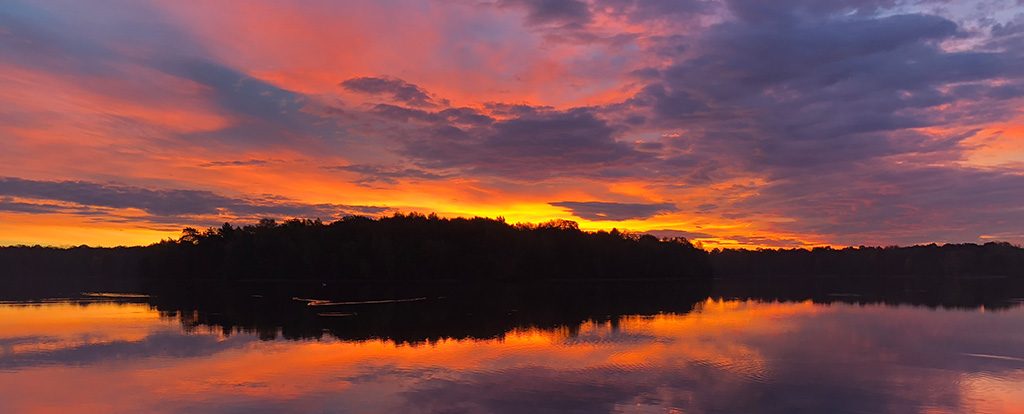 Ein rot glühender Himmel über den Bäumen einer Insel in einem See ist zu sehen. Jeder Sonnenaufgang ist ein Wunder.