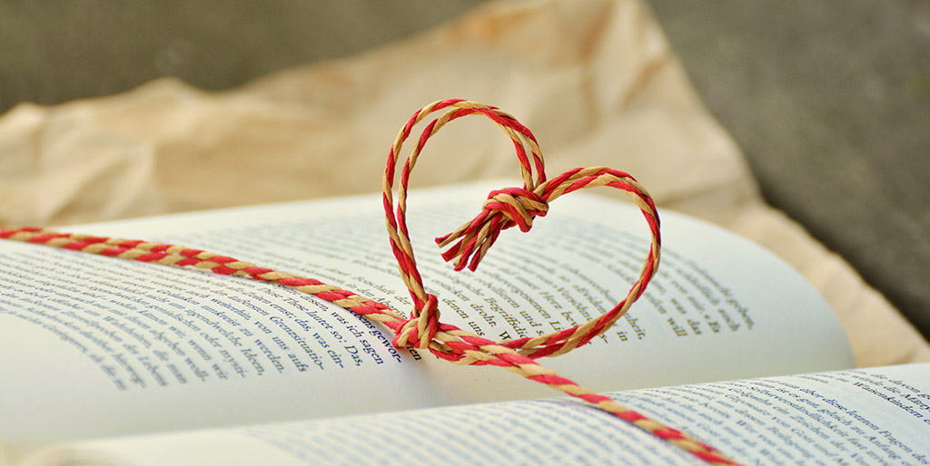 Aus einer zweifarbigen Kordel ist ein Herz geknotet, und liegt mit der Schnur quer über einem Buch.