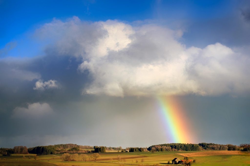 Ein Regenbogen scheint aus einer Wolke zur Erde zu wachsen.