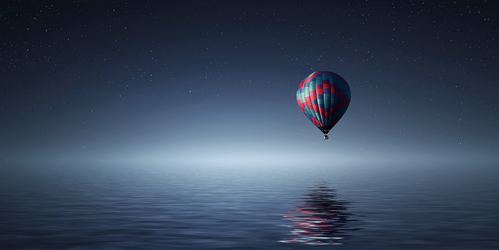 Ein Heißluftballon schwebt bei Nacht über dem Wasser - ein Sinnbild für deine Träume.