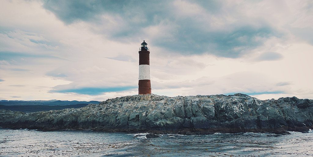 Ein rot-weißer Leuchtturm auf einem Felsen steht im Meer als Symbol für unsere Pflicht anderen gegenüber, in Würde zu leben.